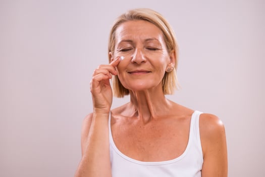 Portrait of beautiful mature woman applying moisturizer on her face. photo