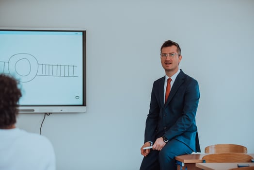 A modernly dressed professor engages in educating students, who listen attentively, creating a dynamic scene of knowledge-sharing and focused learning in the classroom. photo