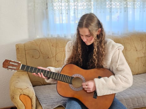 The young, curly-haired girl plays her acoustic guitar with passion and talent in the comfort of her home, creating beautiful melodies in this realistic photograph photo