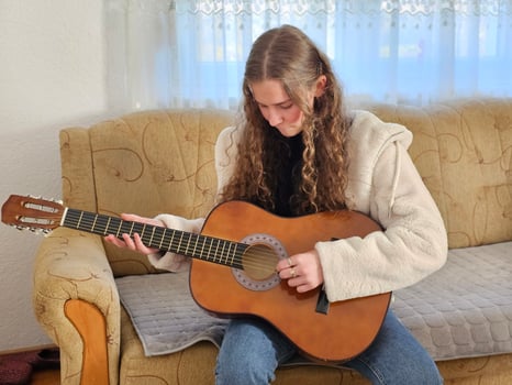 The young, curly-haired girl plays her acoustic guitar with passion and talent in the comfort of her home, creating beautiful melodies in this realistic photograph photo