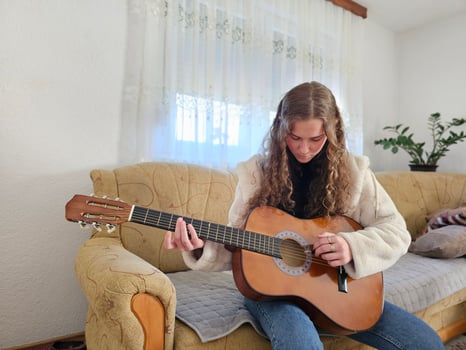The young, curly-haired girl plays her acoustic guitar with passion and talent in the comfort of her home, creating beautiful melodies in this realistic photograph photo