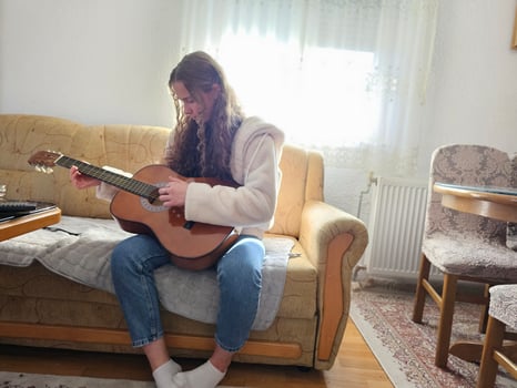 The young, curly-haired girl plays her acoustic guitar with passion and talent in the comfort of her home, creating beautiful melodies in this realistic photograph photo