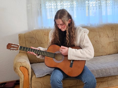 The young, curly-haired girl plays her acoustic guitar with passion and talent in the comfort of her home, creating beautiful melodies in this realistic photograph photo