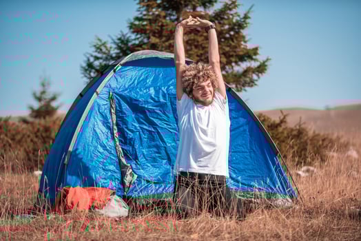 A hiker stretches as he exits his tent on a mountain top, surrounded by picturesque scenery photo