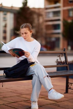 A beautiful blonde teenager sits on a bench in the park, taking a break from school to immerse herself in a book, accompanied by her school backpack photo