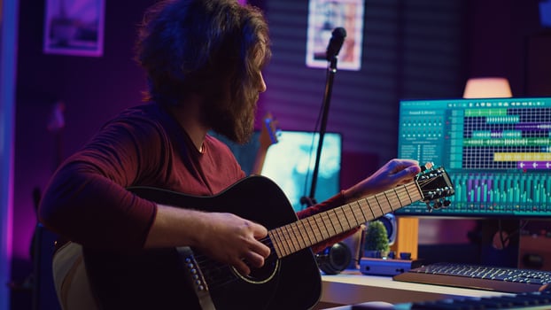 Music producer tuning his acoustic guitar before playing instrument, recording and mixing tunes to create new soundtracks. Singer composing a song using electronic panel controls. Camera B. photo
