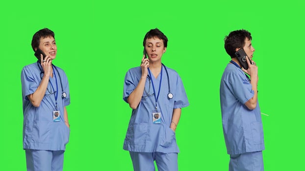 Health specialist using smartphone to make important calls, standing against greenscreen backdrop. Nurse talking to patients for checkup exams on telephone line, calling people to confirm. Camera B. photo