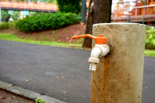 Orange and white colored plastic water faucet isolated on horizontal ratio outdoor park and garden environment with green grasses, botanical plants, gray asphalt road, and orange bridge background. photo