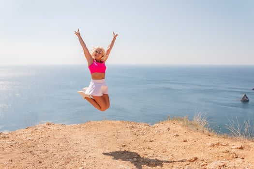 A woman is jumping in the air on a beach with the ocean in the background photo
