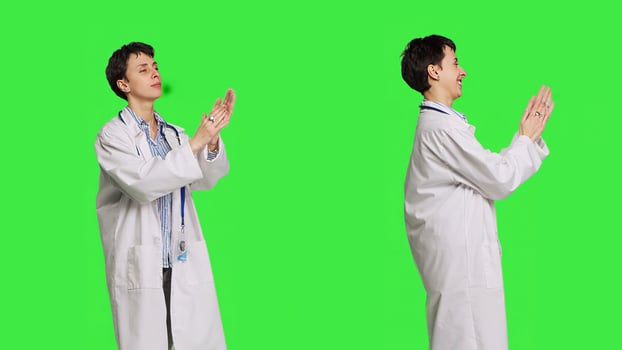 Proud pleased medic applauding colleagues in studio, cheering and feeling happy about their success. Doctor clapping hands and congratulating someone against greenscreen backdrop. Camera B. photo