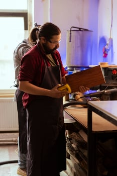 Artisan next to BIPOC coworker using sanding block to remove imperfections on wood piece. Creative person enjoying diy hobby, using sandpaper to do manual sanding near african american colleague photo