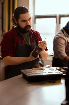 Craftsperson changing power drill head into suitable one for task ahead, making holes into lumber block. Manufacturer in assembly shop preparing electric equipment tool to use for commissioned work photo