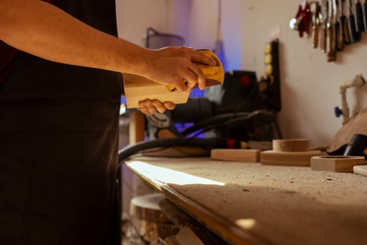 Man working in assembly shop using sanding block to remove imperfections on wood piece. Carpenter using coarse grade sandpaper to do manual sanding, employed in furniture assembly workspace photo