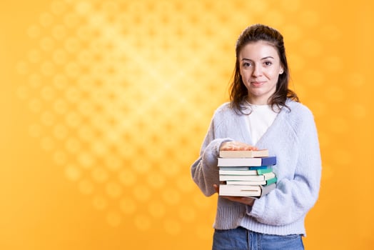 Portrait of woman holding stack of books needed for her education, isolated over studio background. Person using pile of textbooks for knowledge acquisition during academic learning photo