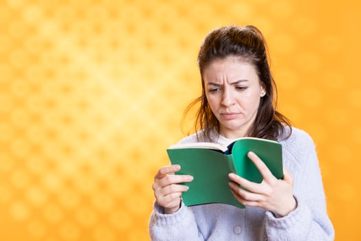 Woman frowns seeing length of lecture book needed for school exam, studio background. Student glares at difficult academic textbook needed to pass classes, feeling troubled and stressed while reading photo