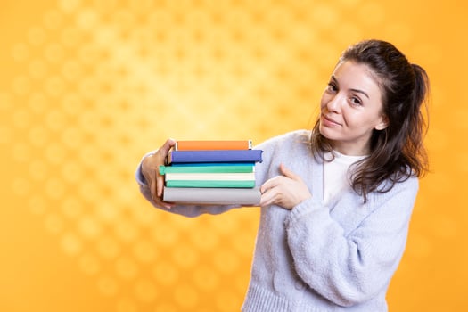 Portrait of upbeat woman holding pile of books, recommending reading, studio background. Radiant person with stack of novels showcasing importance of appreciation for literature photo