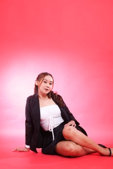 full portrait of young indonesia woman in career office sitting elegantly wearing black jacket, hands to the floor and thighs, for corporate, fashion, commercial, agency content photo