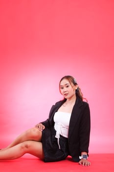 full portrait of mature Asian woman in career office sitting elegantly wearing black suit, hands to thighs and floor, for corporate, fashion, commercial, agency content photo