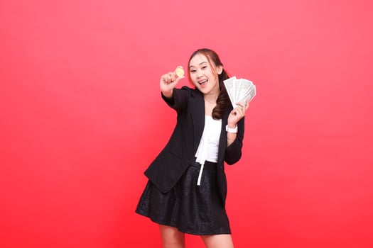 gesture of cheerful young Asian office woman wearing black formal suit, hands holding dollar bills and bitcoins in front of her, for financial content, business, advertising, investment photo