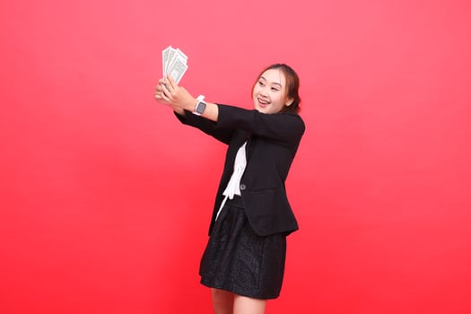 gesture of happy young indonesia office woman wearing formal black suit both hands holding dollar bills in front of right, for corporate content, fashion, advertising, broadcast photo