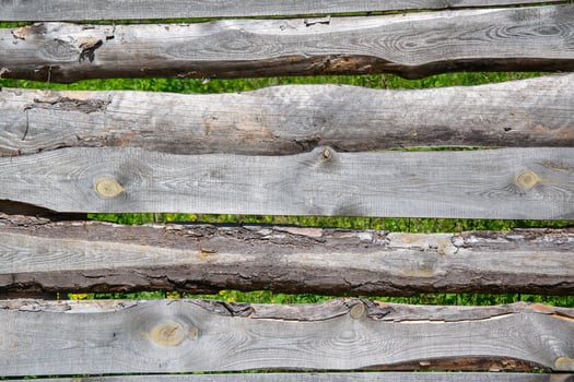 A close-up view of a wooden fence constructed from weathered logs, showcasing knots and grain patterns photo