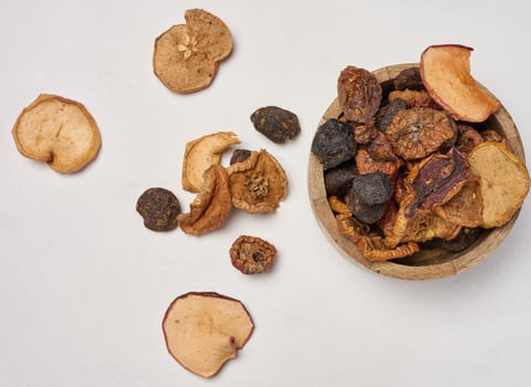 Dried apple pieces in a wooden round plate on a white table, top view photo
