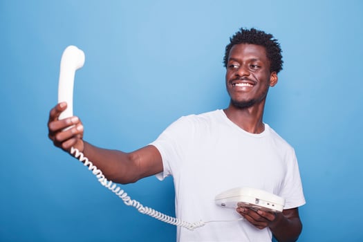 African american gentleman with a smile is holding and looking at the landline phone cord. Black guy with afro standing and grasping a telephone before having a conversation. photo
