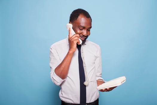 Black businessman holding receiver to ear and talking on landline telephone while listening to person speaking at other end of call. African American employee in white shirt using old school phone. photo