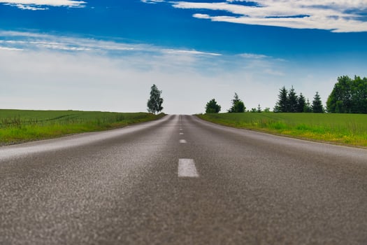 Empty asphalt road leading into horizon under blue sky with clouds and green fields photo