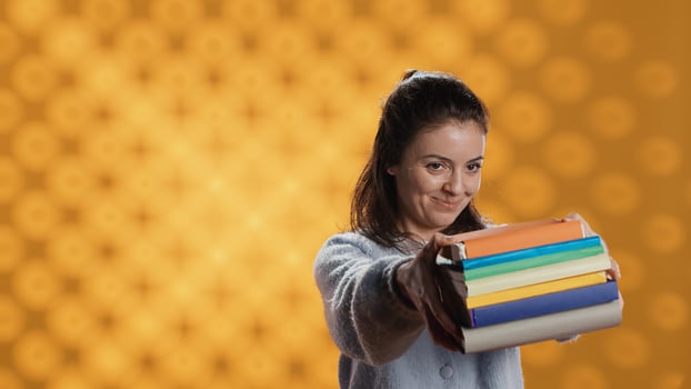 Portrait of friendly woman offering stack of textbooks useful for school exam, isolated over studio background. Merry person giving pile of books, recommending them for university assessment, camera A photo