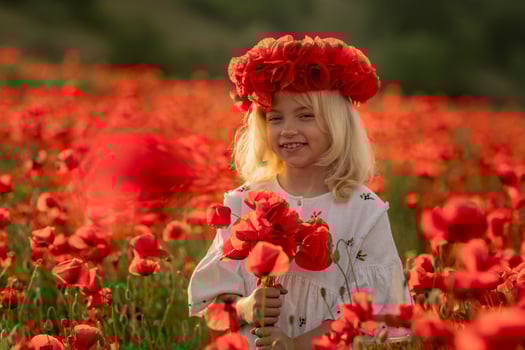A young girl is standing in a field of red flowers, wearing a red flower crown. She is smiling and holding a bouquet of red flowers. Concept of joy and innocence. photo