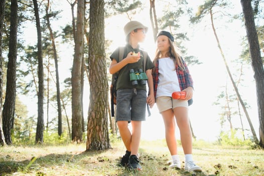 Happy excited school children with backpacks in casual clothes enjoying walk in forest on sunny autumn day, two active kids boy and girl running and playing together during camping trip in nature. photo