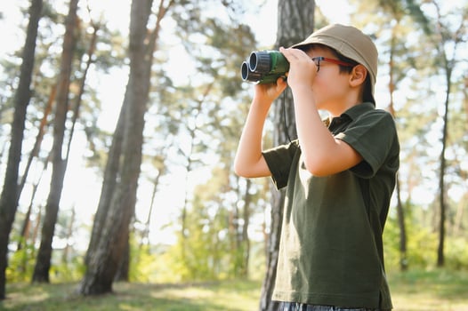 Little boy scout with binoculars during hiking in autumn forest. Concepts of adventure, scouting and hiking tourism for kids. photo