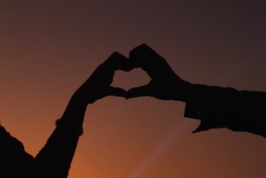 Silhouette of a pair of raised hands forming a heart shape on a beautiful evening landscape background Hand made heart symbol idea showing love friendship and kindness to couples and friends. photo