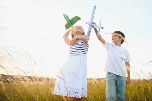 Running boy and girl holding two green and blue airplanes toy in the field during summer sunny day photo