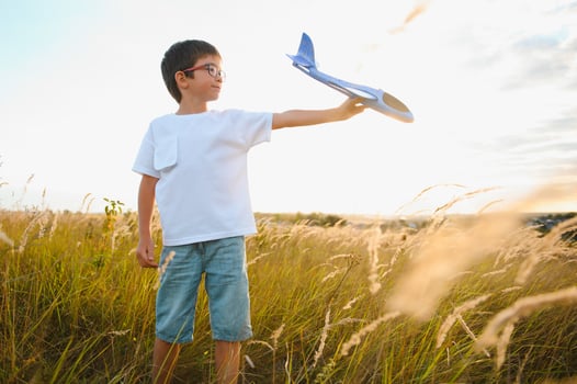 Cute happy cheerful child running fastly along grassy hill at countryside holding big toy plane in hand. Boy playing during sunset time in evening. Horizontal color photography. photo