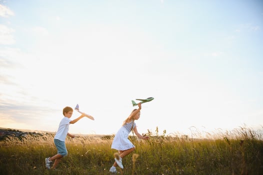 Running boy and girl holding two green and blue airplanes toy in the field during summer sunny day photo