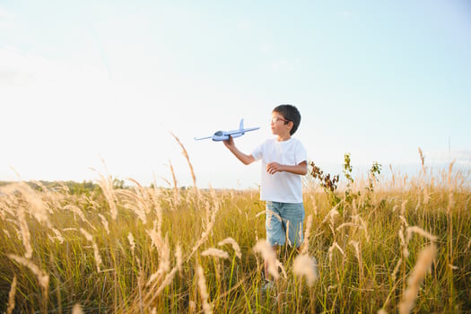 Cute happy cheerful child running fastly along grassy hill at countryside holding big toy plane in hand. Boy playing during sunset time in evening. Horizontal color photography. photo