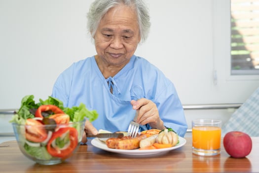 Asian senio woman patient enjoy eating breakfast with vegetable healthy food while sitting and hungry on bed in hospital. photo