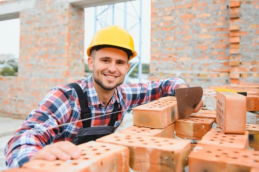 Using bricks. Young construction worker in uniform is busy at the unfinished building photo