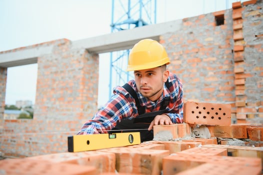 Using bricks. Young construction worker in uniform is busy at the unfinished building photo