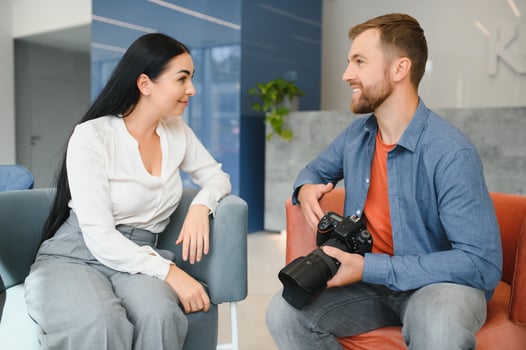 Photographer in office shows photo model in camera. Consultant adjusts activities company as whole. Photo session employees in workplace. Manager well-executed project. Photos best employees company.