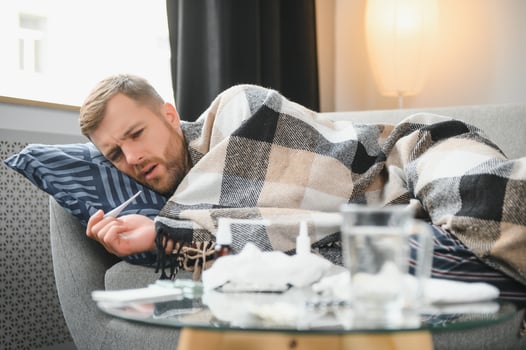 It's cold at home in wintertime. Man freezing in his house in winter because of broken thermostat. young guy wrapped in woolen plaid shivering while sitting on sofa in living room interior photo