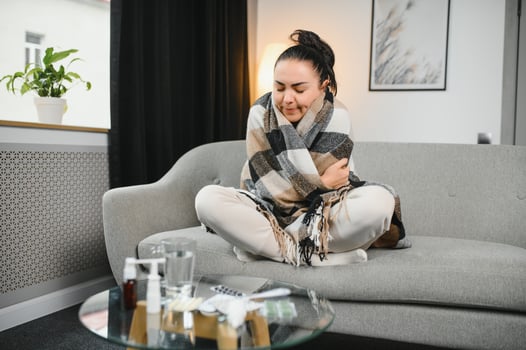 Sick woman with a headache sitting on a sofa at home wrapped in grey blanket photo