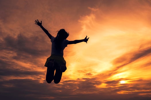 Silhouette young woman jumping outstretched hands in colorful sunset sky photo