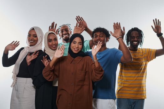 A jubilant and diverse group, including an African American man and hijab-wearing girls, exuberantly wave and celebrate, embodying the vibrancy of student life against a white backdrop, symbolizing photo
