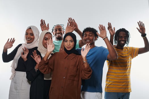 A jubilant and diverse group, including an African American man and hijab-wearing girls, exuberantly wave and celebrate, embodying the vibrancy of student life against a white backdrop, symbolizing photo
