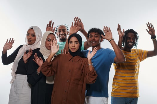 A jubilant and diverse group, including an African American man and hijab-wearing girls, exuberantly wave and celebrate, embodying the vibrancy of student life against a white backdrop, symbolizing photo
