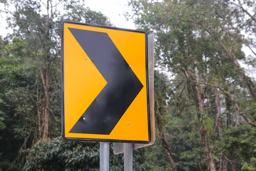Yellow and Black Arrow Road Sign with Trees in the Background photo