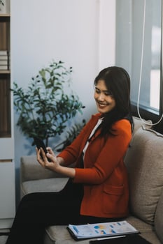 Smiling and happy millennial Asian businesswoman chatting with her friends on her phone, scrolling on social media or watching on the internet, using her phone while relaxing in the office. photo